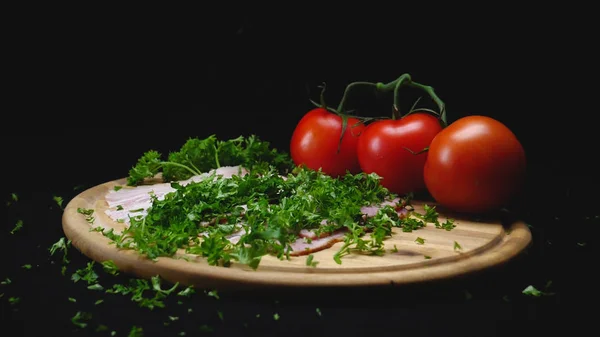 Nahaufnahme von Zutaten auf hölzernem Kochbrett auf schwarzem, isolierten Hintergrund. Rahmen. Eine Handvoll grüne, duftende Petersilie ergießt sich über Fleischscheiben. fettes Fleisch durch saftiges Grünzeug ersetzen — Stockfoto