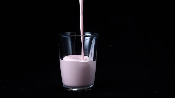 Полуничне молоко трясеться ізольовано на чорному тлі. У прозоре скло наливають в'язкий рожевий молочний коктейль на чорний фон. Прохолодні молочні коктейлі — стокове фото