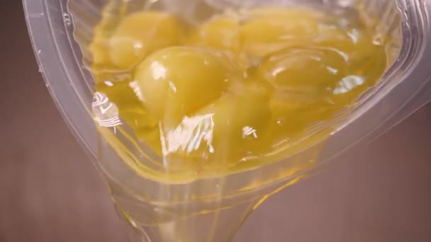 Närbild av råa ägg hälls från koppen. Stock film. Råa ägg med äggula och proteiner spridda från plastbehållare för bakning — Stockvideo