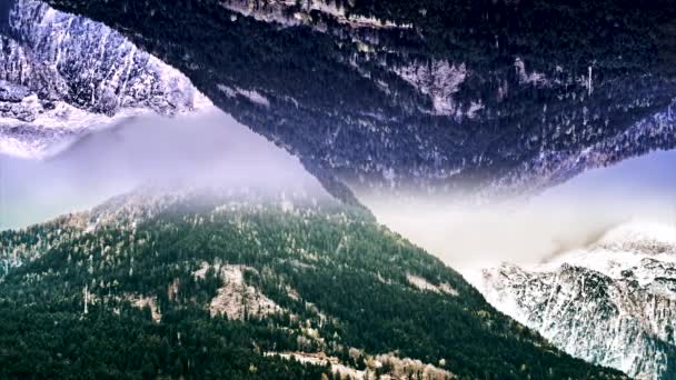 Abstrakte Luftlandschaft zweier schneebedeckter Berge mit Spiegeleffekt. Animation. surreale verkehrt herum gespiegelte Welt, winterbewaldete Felsen in Wolken, Gründungsthema. — Stockvideo