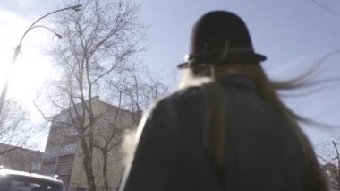 Şehirde yürüyen geniş kenarlı şapka ve siyah deri ceket genç bir güzel model kız Arka görünümü. Eylem. Dinamik genç kız rüzgarda onu adil çırpınan ile sokakta yürüyor.