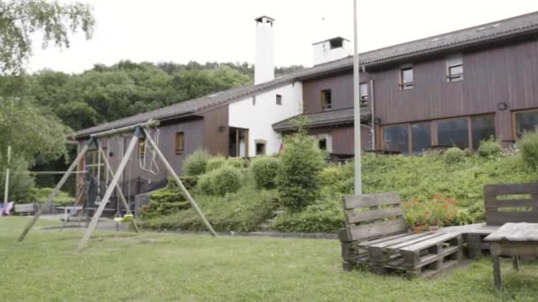 Bel extérieur vert d'une maison moderne sur fond de ciel gris. L'action. Cour avec gazon vert et patio, balançoire et table avec bancs en bois . — Video