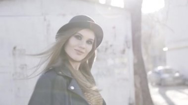 Şapkalı ve modaya uygun siyah ceketli seksi modern hippi kadın klasik bir binanın yakınındaki bir sokakta kalıyor. Başla. Dışarıda akşam güneşinde kameraya poz veren sevimli bir kız..