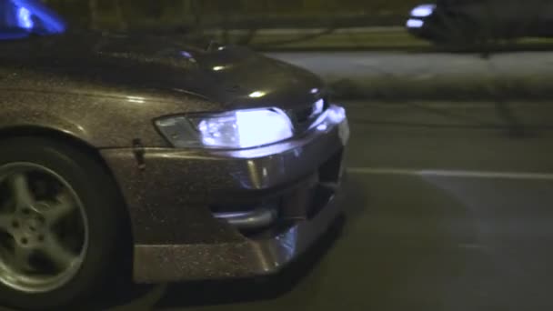 Vista laterale di una macchina che guida lungo la strada, fari che illuminano la strada buia di notte. Azione. Paraurti anteriore auto lilla sintonizzato con fari al neon bianco . — Video Stock