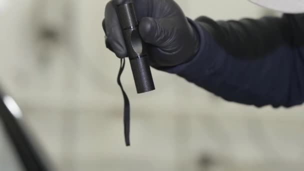 Närbild för manlig hand i svart handske som håller svart ficklampa med smal balk i reparations butiken. Åtgärder. Man håller liten ficklampa under arbetsprocessen. — Stockvideo