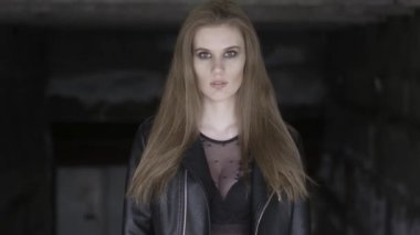 Siyah kentsel arka plan üzerinde duran, şık siyah kıyafet giyen düz uzun kahverengi saçlı güzel genç kadın Portresi. Eylem. Siyah dumanlı gözleri olan bir kız kameraya bakıyor.