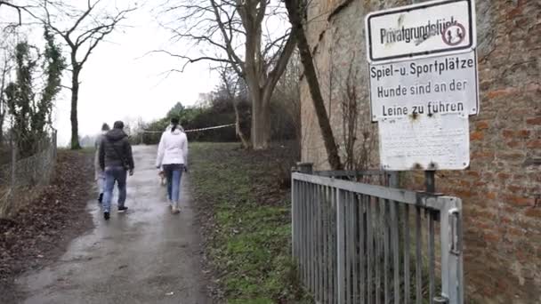 Rear view of hikers on a hiking trail going near bare trees and brick building. Art. Group of people moving on a path withered grass, nature after the rain. — ストック動画