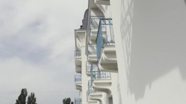 Modern yapının mavi ferforje korkuluklu balkonların yan görünümü, mimari arka plan. Eylem. Bulutlu gökyüzüne karşı balkonlu bir evin beyaz duvarı.
