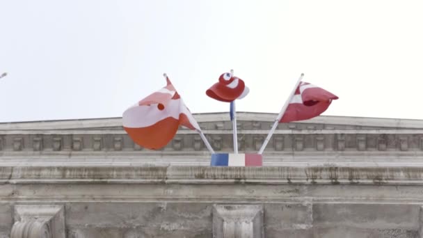Uitzicht van beneden naar een oud gebouw met vlaggen zwaaiend in de wind op Bright Sky achtergrond, Frankrijk. Actie. Verschillende vlaggen fladderen in de wind op de ambassade. — Stockvideo