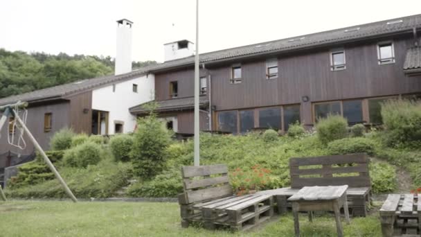 Beautiful green exterior of a modern house on grey sky background in rainy weather. Action. Yard with green grass and patio area, swing and table with wooden benches. — Stock Video