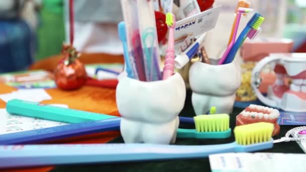 Zblízka pro zubařské nástroje ve skleněném šálku ve tvaru zubu a barevné zubní kartáčky na zubní klinice, koncept dětské medicíny. Umění. Model lidských plastových zubů na stole. — Stock video