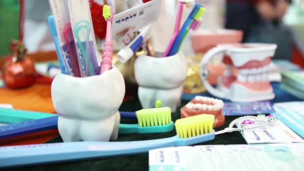 Cierre para arriba para las herramientas del dentista en taza en forma de diente de vidrio y cepillos de dientes de colores en una clínica dental, concepto de medicina para niños. Art. Modelo de dientes de plástico humano sobre la mesa . — Vídeos de Stock