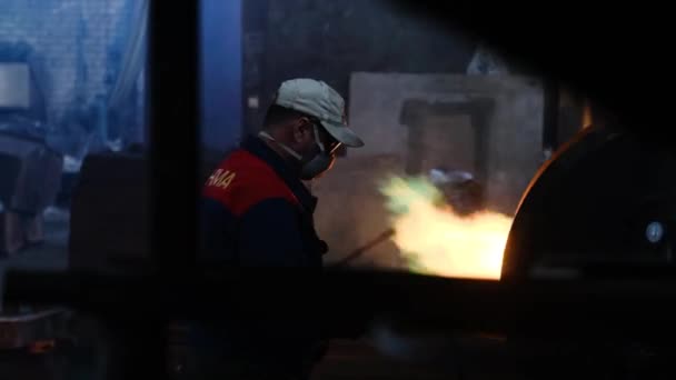 작업자는 공장에서 화재로 용광로에서 금속을 녹입니다. 스톡 푸티지. 녹색 언어로 화염을 상승하는 용광로에서 금속을 녹이는 헬멧 경찰의 형태로 노동자 — 비디오