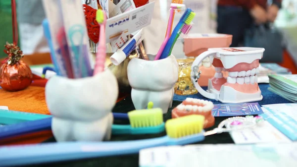 Zblízka pro zubařské nástroje ve skleněném šálku ve tvaru zubu a barevné zubní kartáčky na zubní klinice, koncept dětské medicíny. Umění. Model lidských plastových zubů na stole. — Stock fotografie