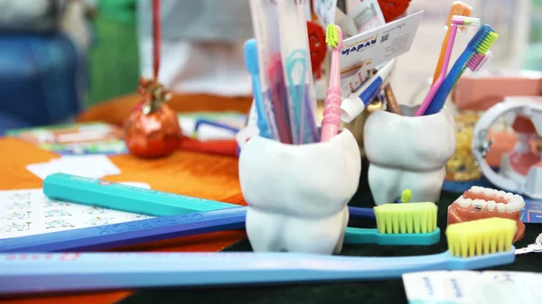 Cierre para arriba para las herramientas del dentista en taza en forma de diente de vidrio y cepillos de dientes de colores en una clínica dental, concepto de medicina para niños. Art. Modelo de dientes de plástico humano sobre la mesa . — Foto de Stock