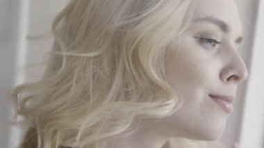 Pencereden dışarı bakan gülümseyen bir kadının portresini yakından çek. Başla. Kıvırcık saçlı, güzel sarışın kız yan bakıp bir şeyler düşünüyor..