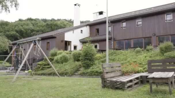 Patio bellamente diseñado cerca de la casa de madera moderna en tiempo lluvioso. Acción. Patio trasero con bancos y mesa hechos a mano y el columpio en el prado verde . — Vídeo de stock