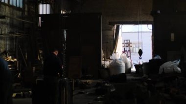 İşçiler bitkinin eski deposunda çalışır. Stok görüntüleri. Fabrika işçileri açık kapılar arka planda eski depo dağınık odasında temizlenir