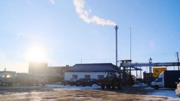 Beskåda av platsen av den industriella växten på bakgrund av blått skyen. Stock film. Traktor lämnar industriellt skyddat område mot blå himmel med ljus sol — Stockvideo