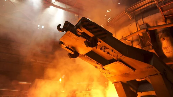 Um mecanismo com ganchos na loja quente com aumento de fumaça e queima de fogo na planta metalúrgica. Imagens de stock. Indústria pesada, equipamentos na fábrica de aço . — Fotografia de Stock