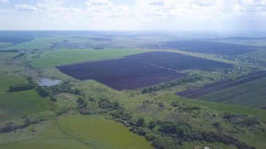 Pürüzlü ve yeşil tarlaların, ağaçların, arka planda mavi bulutlu gökyüzünün olduğu küçük bir kasabanın hava aracı görüntüsü, tarım kavramı. Şarjör. Yazın İngiliz kırsal arazisi.