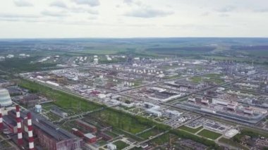 Yeşil tarlaları ve arka planında bulutlu gökyüzü olan petrol ve gaz kimya tesisi. Şarjör. Yeşil pirinç tarlalarının ve köy yollarının yanındaki fabrikada baca tüttürmek.
