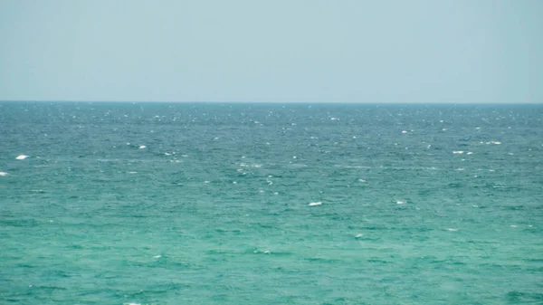 Όμορφο θαλασσινό τοπίο, νερό με μικρά κύματα, ατελείωτος ορίζοντας, και καθαρός, γαλάζιος ουρανός. Πυροβολήθηκε. Τυρκουάζ νερά με μικρούς κυματισμούς σε μια καλοκαιρινή, ηλιόλουστη μέρα. — Φωτογραφία Αρχείου
