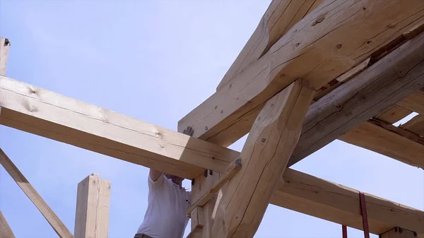 Workers build and stack boards wooden house. Clip. Workers install beautiful wooden beams on construction site of house. Wooden house in mode of construction on background of sky