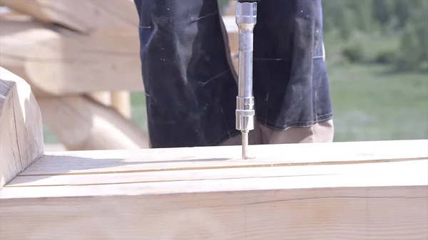 Close-up of worker drills wooden board. Clip. Carpenter drills log with special drill for construction of wooden house