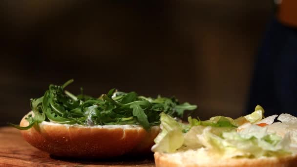 Cocine añadiendo lechuga en la hamburguesa. Imágenes de archivo. Preparando hamburguesa. Cocinar las manos preparando y haciendo hamburguesa — Vídeos de Stock