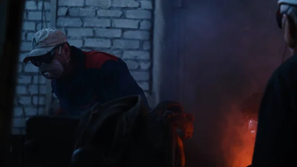 Workers at metallurgical plant working with hot metal. Stock footage. Workers in uniforms and helmets work with dangerous hot metal at high temperatures in old metallurgical factory