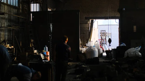 Les travailleurs travaillent dans l'ancien entrepôt de l'usine. Images d'archives. Les ouvriers d'usine sont nettoyés dans la pièce encombrée du vieil entrepôt sur fond de portes ouvertes — Photo