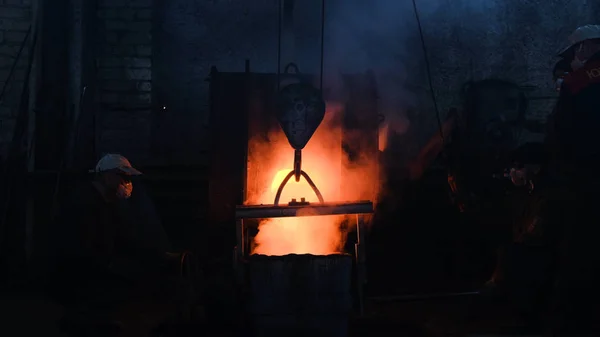 Werknemers schonk gesmolten metaal in de plant. Stock footage. Werknemers in vorm en helmen controleproces van het gieten van gesmolten metaal van ketel bij metallurgische plant — Stockfoto