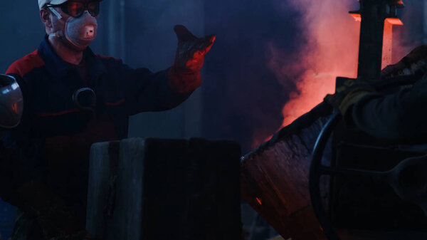 Workers poured molten metal at plant. Stock footage. Workers in form and helmets control process of pouring molten metal from boiler at metallurgical plant