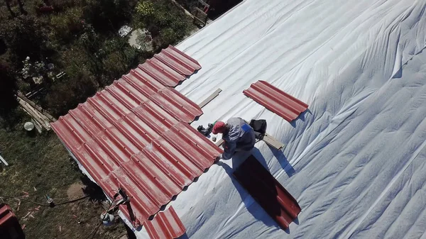 Hombre haciendo techo de casa de campo. Imágenes de archivo. Vista superior del constructor poniendo tejas de metal en el techo. El hombre instala independientemente recubrimiento en el techo con poco viento, que no es muy seguro —  Fotos de Stock