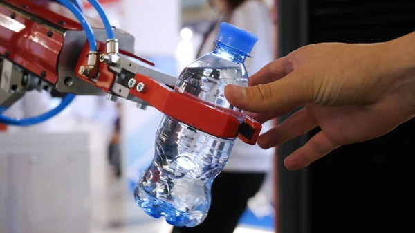Robot hand is holding a bottle of water. Media. Technological progress. Robotic arm holds a water bottle