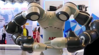 Endüstriyel robot makinesi endüstriyel uluslararası sergide, bilim konsepti. Medya. Arka planda hareket eden insanlarla kollarını hareket ettiren bir robot için yakın çekim.