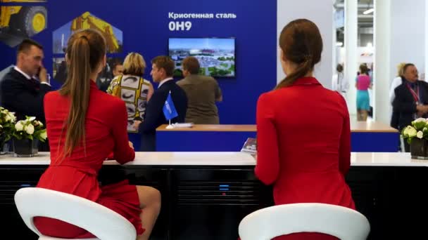 Rear view of two women in red jackets sitting at bar counter and putting notebooks on it at the exhibition. Media. Girls in red suits and with ponytails working at the exhibition. — Stock Video