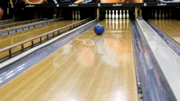 Bola de bolos azul y bolos blancos de pie en una bolera de madera, concepto de juegos deportivos activos. Medios. Bola azul rodando en el carril y derribando alfileres blancos . — Vídeos de Stock