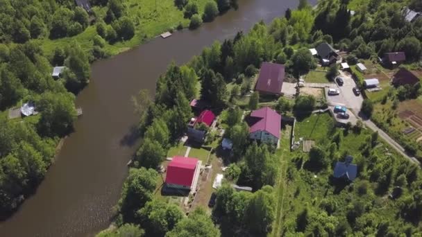 Widok z lotu ptaka pięknej małej rosyjskiej wioski i podmiejskich domów nad wodą. Klip. Zapierające dech w piersiach zalesiony obszar z domków i słońce odzwierciedlenie w wąskiej rzece. — Wideo stockowe