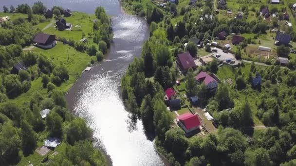 Vista aérea de uma bela pequena aldeia russa e casas suburbanas à beira-mar. Clipe. Área florestada de tirar o fôlego com chalés e o sol refletido no rio estreito . — Vídeo de Stock