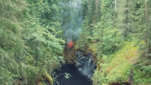 Vista aérea del hombre de pie en el borde del barranco profundo con destello de señal roja en su mano en el bosque cerca de los árboles y arbustos altos y viejos. Imágenes de archivo. Señales SOS en el bosque — Vídeo de stock