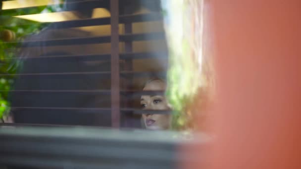 Mladá žena se dívá z okna domu. Článek. Krásná blondýnka s pohledem z okna — Stock video