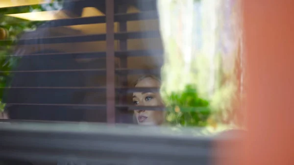 Una giovane donna guarda fuori dalla finestra della casa. Art. Bella bionda che guarda fuori dalla finestra — Foto Stock