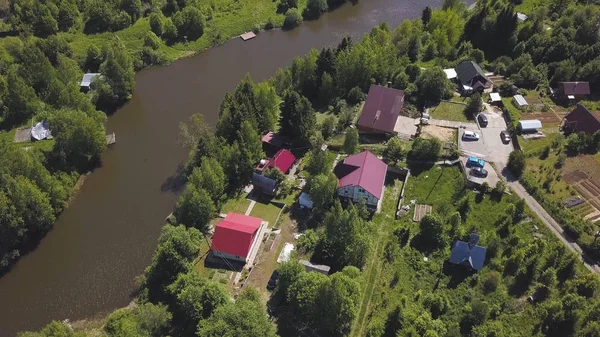 Luftaufnahme eines schönen kleinen russischen Dorfes und vorstädtischer Häuser am Wasser. Clip. Atemberaubendes Waldgebiet mit Hütten und der Sonne, die sich in einem schmalen Fluss spiegelt. — Stockfoto