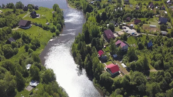 Luftaufnahme eines schönen kleinen russischen Dorfes und vorstädtischer Häuser am Wasser. Clip. Atemberaubendes Waldgebiet mit Hütten und der Sonne, die sich in einem schmalen Fluss spiegelt. — Stockfoto