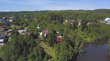 Bir sürü yeşil ağacı ve yaz gökyüzünün altında bir yol olan banliyö bölgesinin havadan görünüşü. Şarjör. Nehir kıyısındaki ormanlık tepelerin arasında küçük bir kasaba..