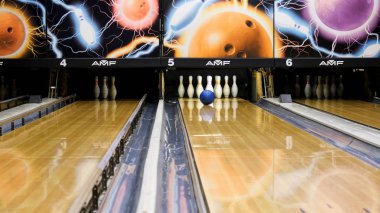 Mavi bowling topu ve beyaz skittles ahşap bir bowling salonu, aktif spor oyunları kavramı üzerinde duran. Medya. Mavi top şeritte yuvarlanan ve beyaz pimleri deviren.