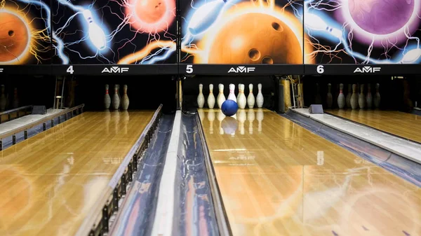 Mavi bowling topu ve beyaz skittles ahşap bir bowling salonu, aktif spor oyunları kavramı üzerinde duran. Medya. Mavi top şeritte yuvarlanan ve beyaz pimleri deviren.