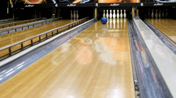 Palla da bowling blu e birilli bianchi in piedi su una pista da bowling in legno, concetto di giochi sportivi attivi. I media. Palla blu che rotola sulla corsia e abbatte i birilli bianchi . — Foto Stock